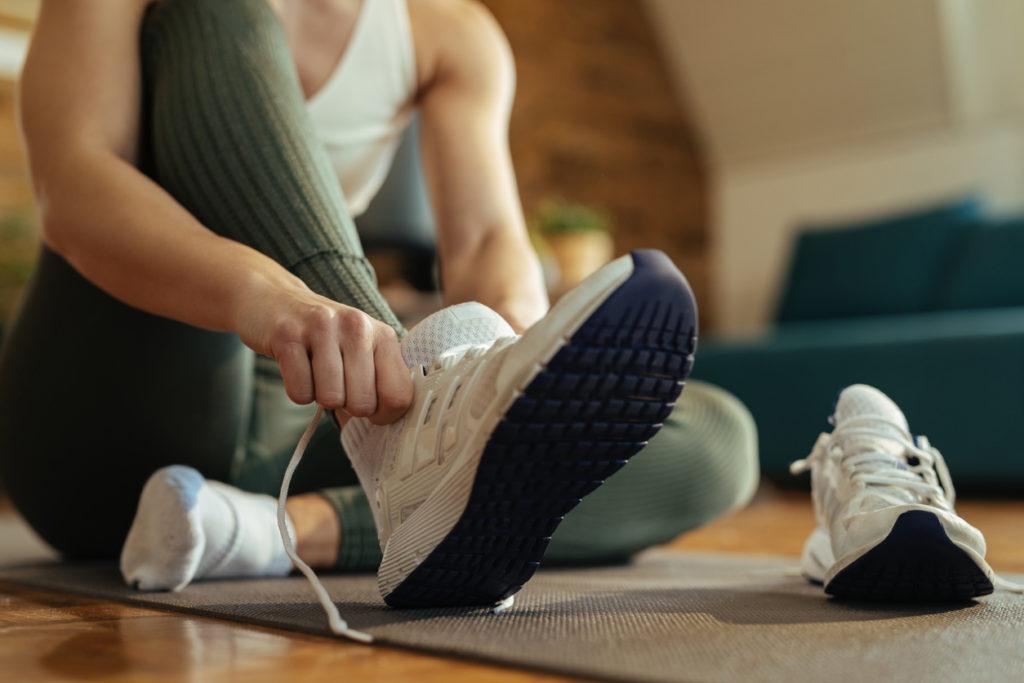 Woman at home putting on a pair of white running shoes before working out.