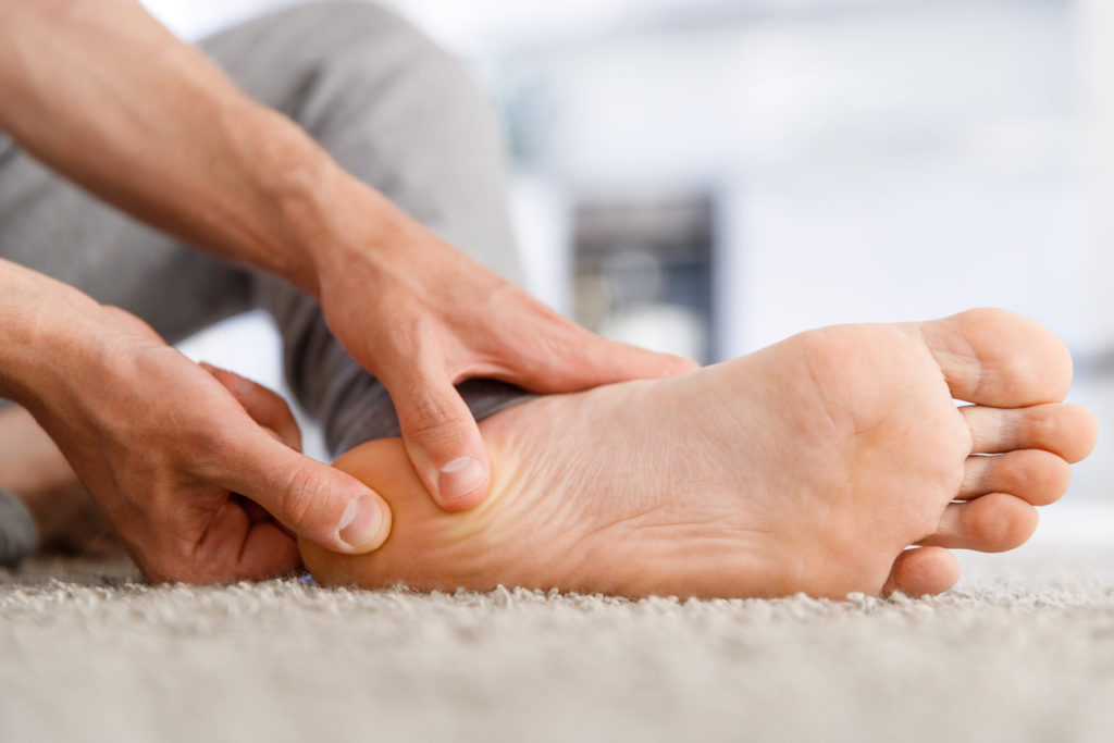 Man suffering from plantar fasciitis, massaging the heel part of his left foot.