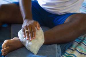 Man at home putting a pack of ice on his sprained ankle.