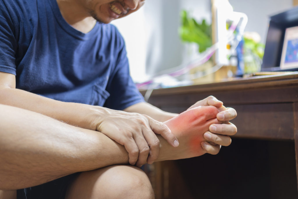 Man experiencing pain from his big toe, holding his right foot - symptoms of turf toe or gout.