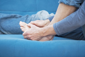 Man at home holding his left toes showing pain coming from his plantar plate injury.