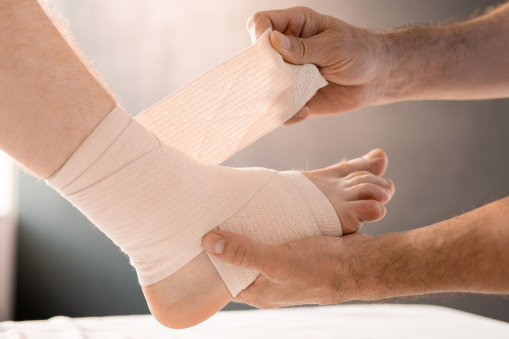 Hands of podiatrist wrapping foot and leg of a patient with a flexible bandage.